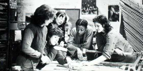 A group of 5 women working on and discussing something related to design.