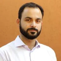 Ivan Marqus is facing the camera. He is wearing a light-colored button-up shirt standing against a yellow background.