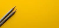 Two grey pencils on a yellow background