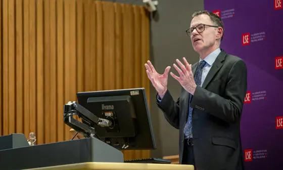 Man in a suits stood in front of an LSE banner and behind a lectern delivering a lecture