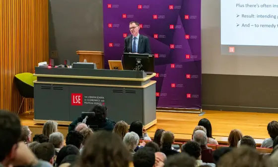Man in a suit delivering a lecture at LSE with the backs of peoples heads in the foreground