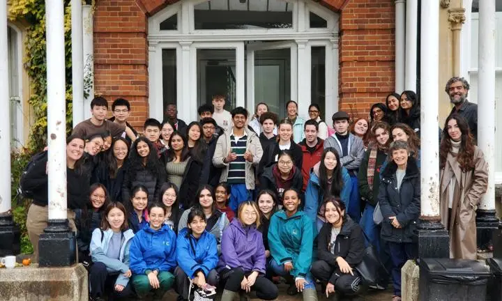 Students and staff standing and sitting next to a door with white pillars at the side.