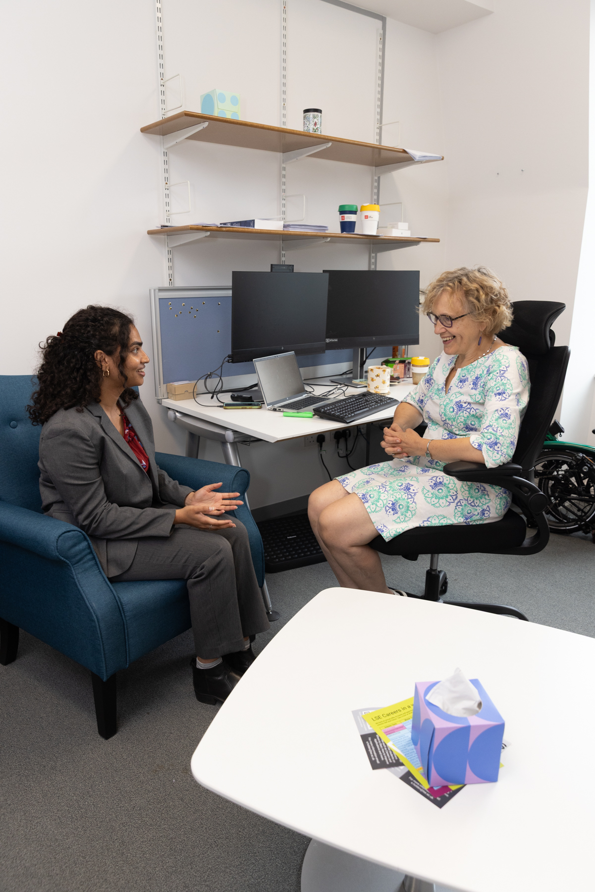 A student in a suit in conversation with a woman in a chair, both sitting and dressed formally