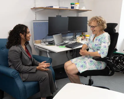 A student in a suit in conversation with a woman in a chair, both sitting and dressed formally