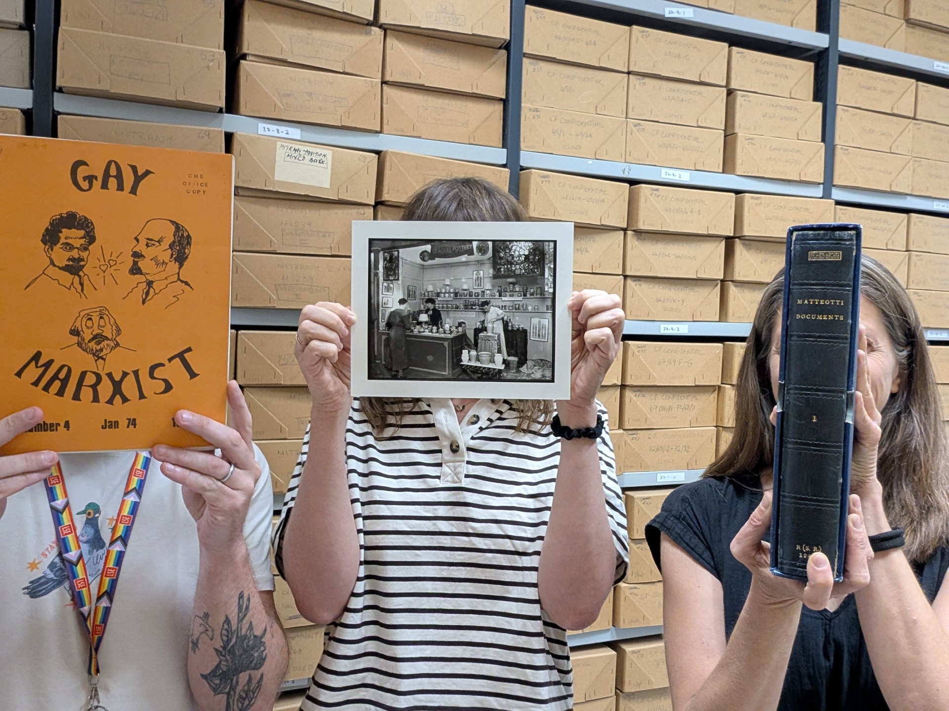 Three people stood holding up exhibits in front of their faces.