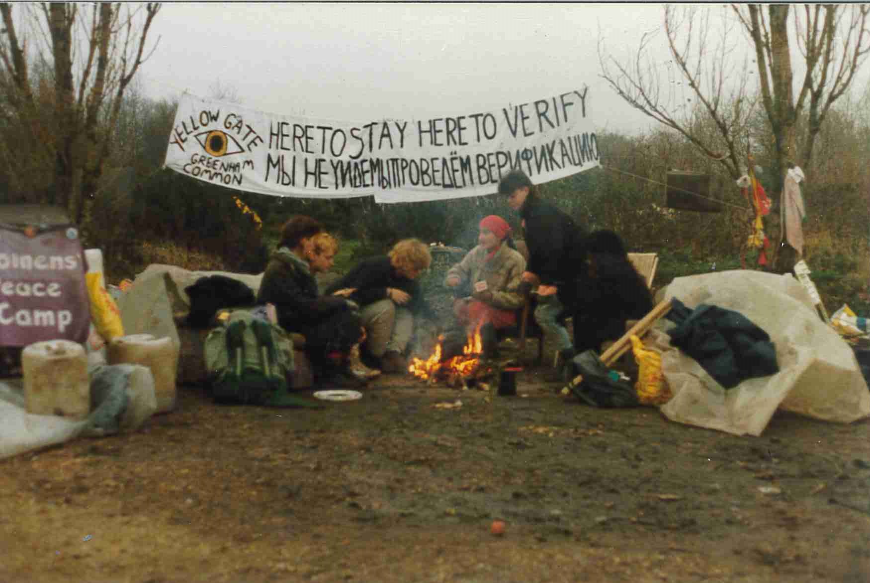 A group of women say at a peace camp with a banner behind them.