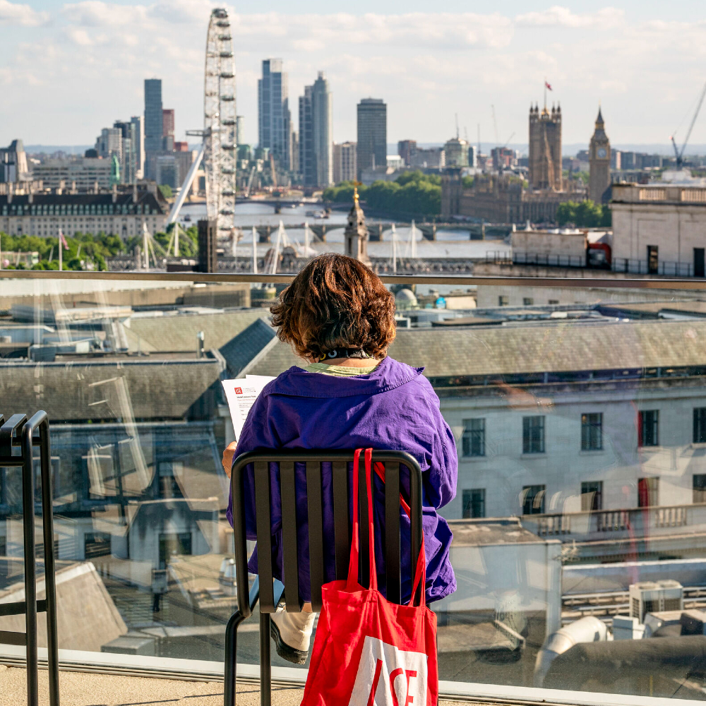  A person sat on a rooftop reading with the London skyline in front of them