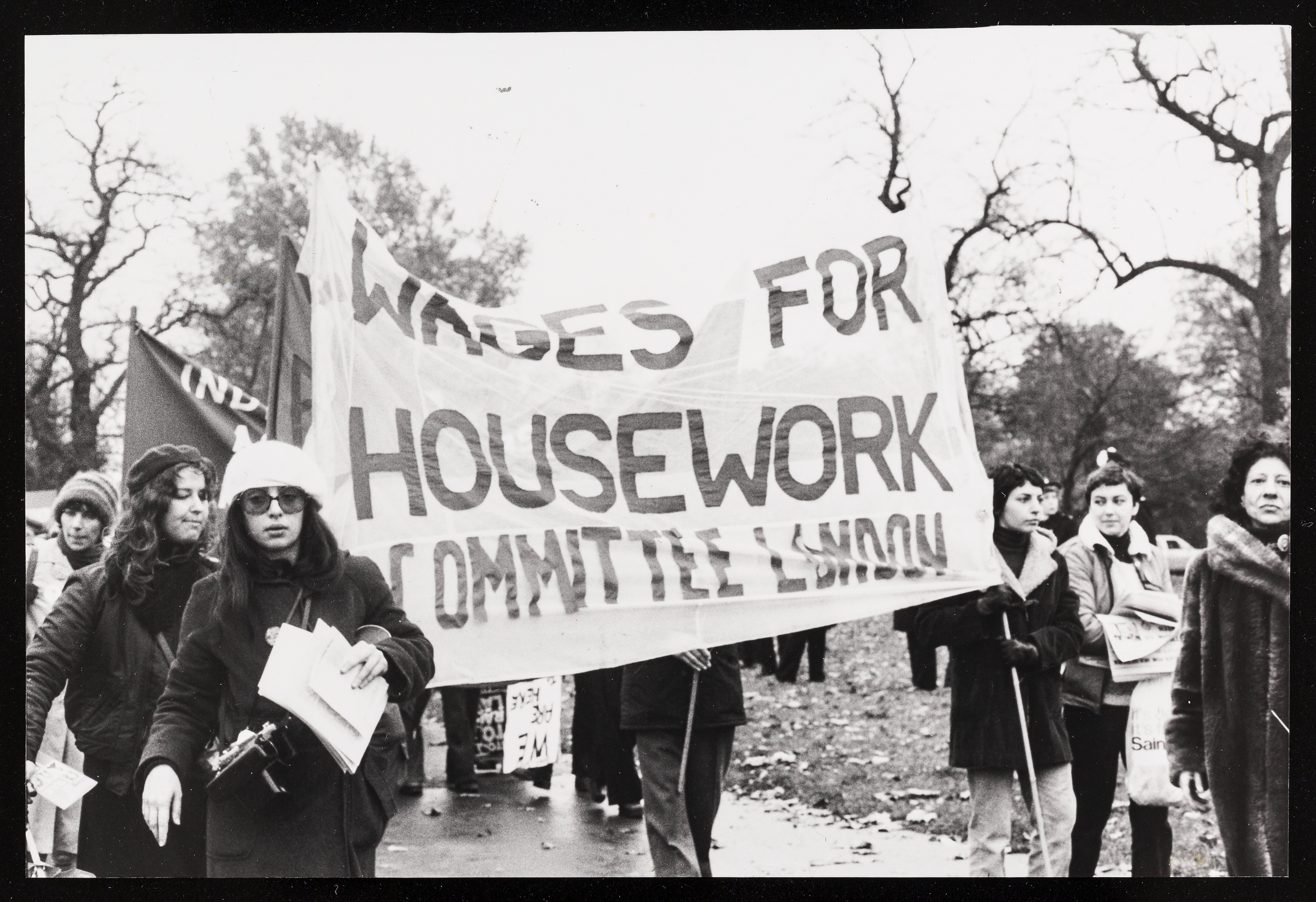 A group of women marching holding a banner reading 'WAGES FOR HOUSEWORK COMMITTEE LONDON'