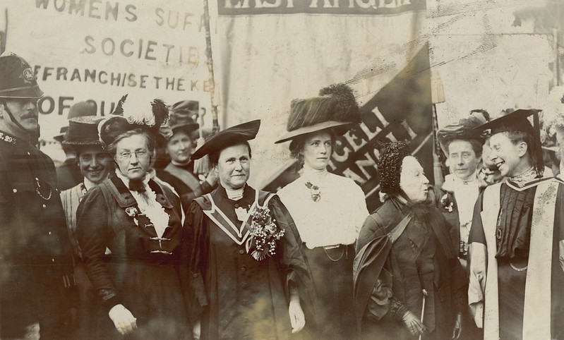 A group of women protesting with banners watched by a police officer.
