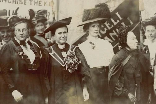 A group of women protesting with banners watched by a police officer.