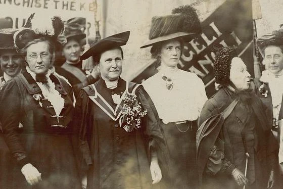 A group of women protesting with banners watched by a police officer.