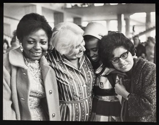 A group portrait of four delegates at the World Congress of Women, Moscow, Jun 1963, standing in a line, embracing.