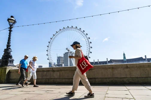 LSE student walking over Waterloo bridge near London South Bank with London Eye in background