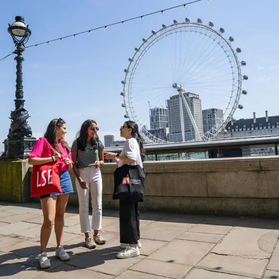 Three LSE students talking near the Thames with the London Eye in the background