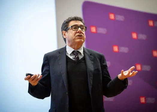 Philippe Aghion addresses the audience. He stands mid-speech with his hands apart. The LSE banner is in the background.