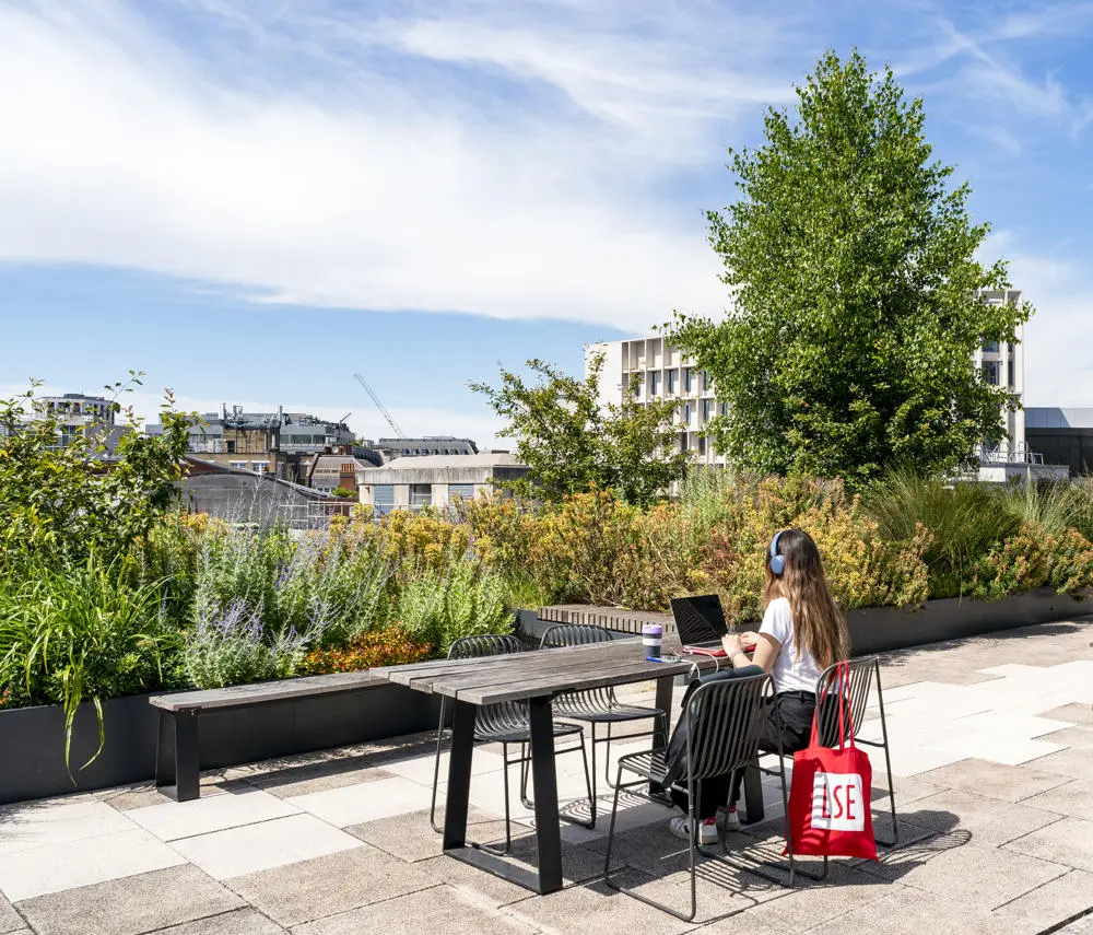 A student working on LSE rooftop with an LSE totebag