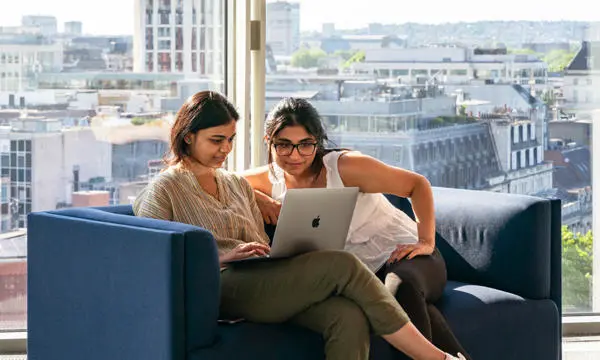 Two students sitting on a sofa, working at laptop.