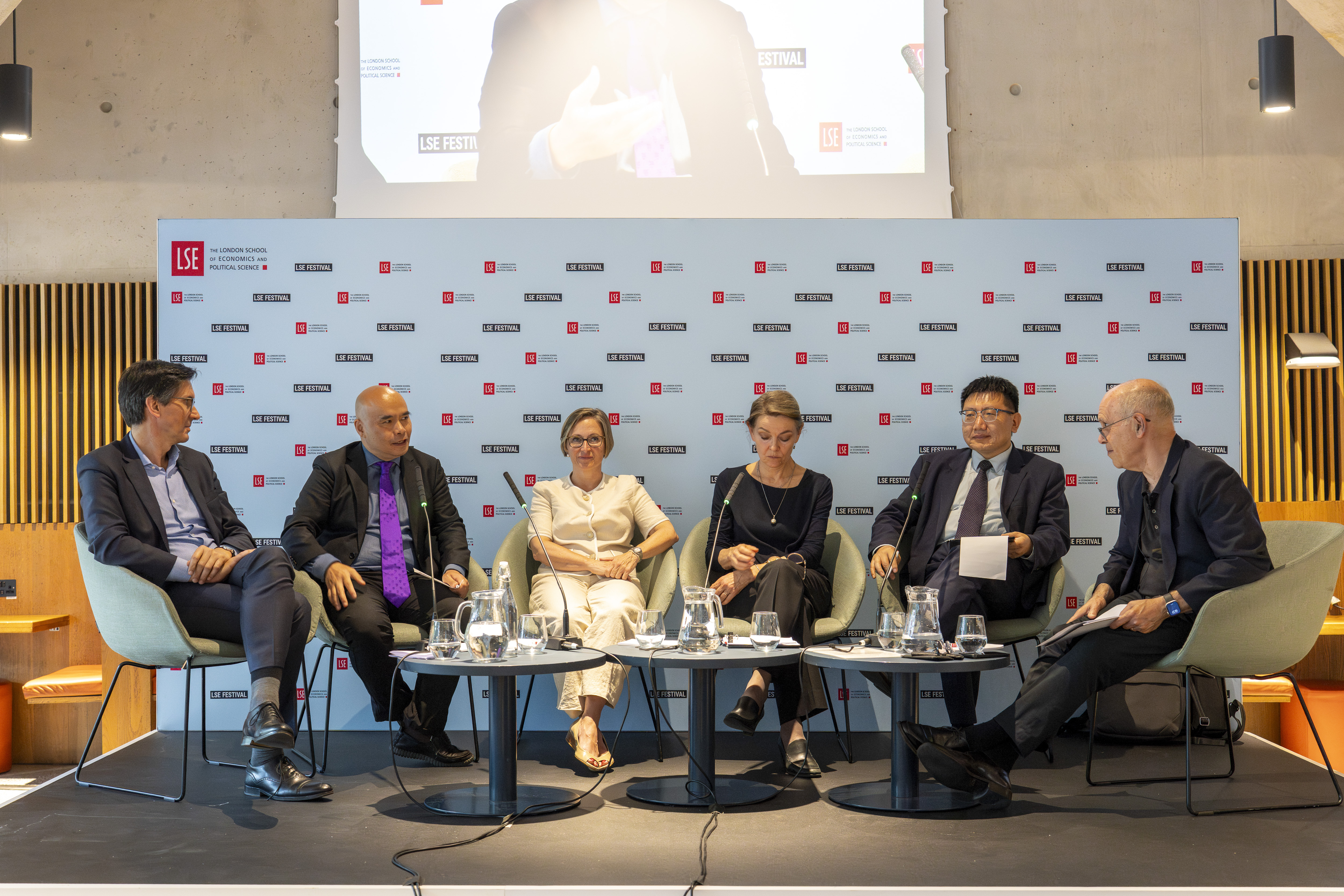 Six individuals sitting in chairs on a stage at the LSE Festival during a panel. 