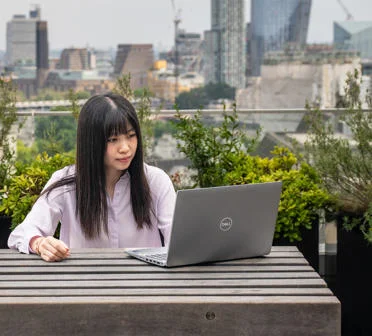 Student using a laptop on a rooftop overlooking central London
