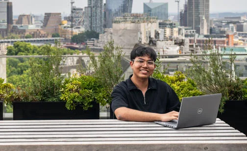 Student using a laptop on a rooftop overlooking central London