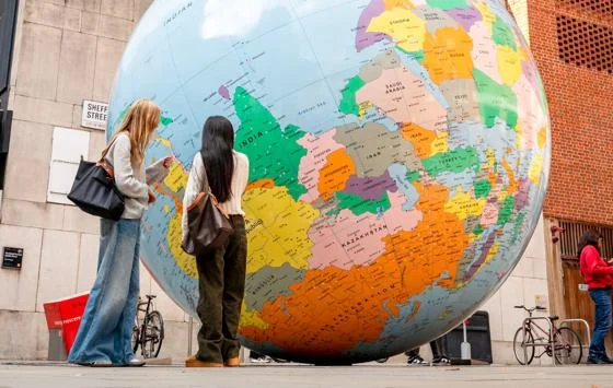 Students standing in front of the LSE Globe with the Peacock Theatre and Saw Swee Hock Building in view.