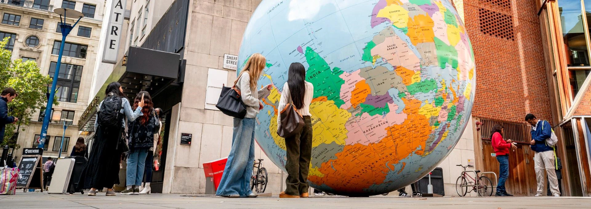 Students standing in front of the LSE Globe with the Peacock Theatre and Saw Swee Hock Building in view.