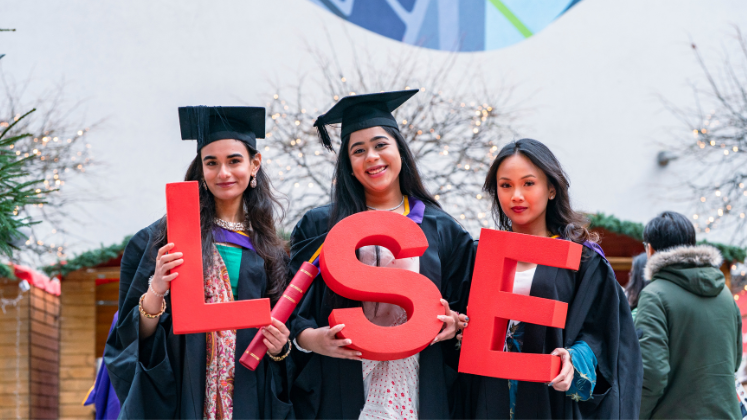 Three female LSE graduates holding LSE letters