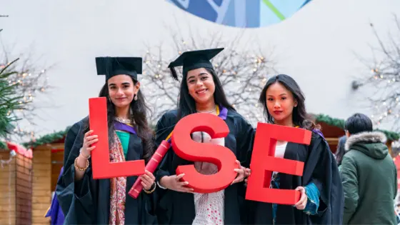 Three female LSE graduates holding LSE letters