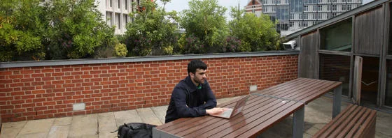 LSE student working on his laptop on the roof terrace of the LSESU Saw Swee Hock Centre