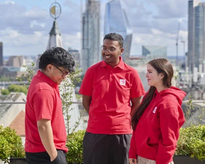 Three student ambassadors in red uniform stood outside laughing