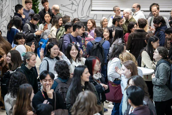 A group of students and staff stand in a room and talk
