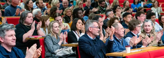 rows of people clapping seated in a lecture theatre