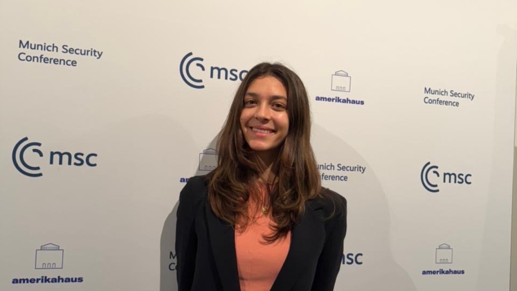 Participant attending the Munich Security Conference, posing in front of official event branding and partner logos.
