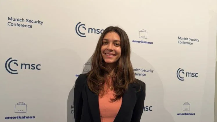 Participant attending the Munich Security Conference, posing in front of official event branding and partner logos.