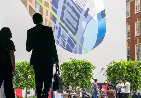 The silhouettes of two people walking across the LSE Centre Building Square