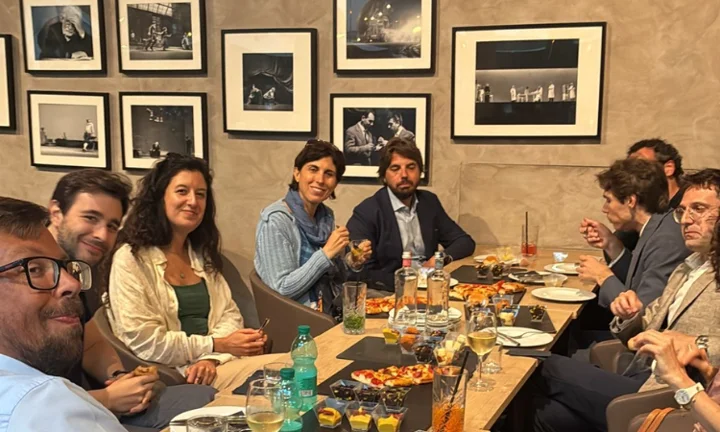 Alumni in Milan gather around a table with food and drink.