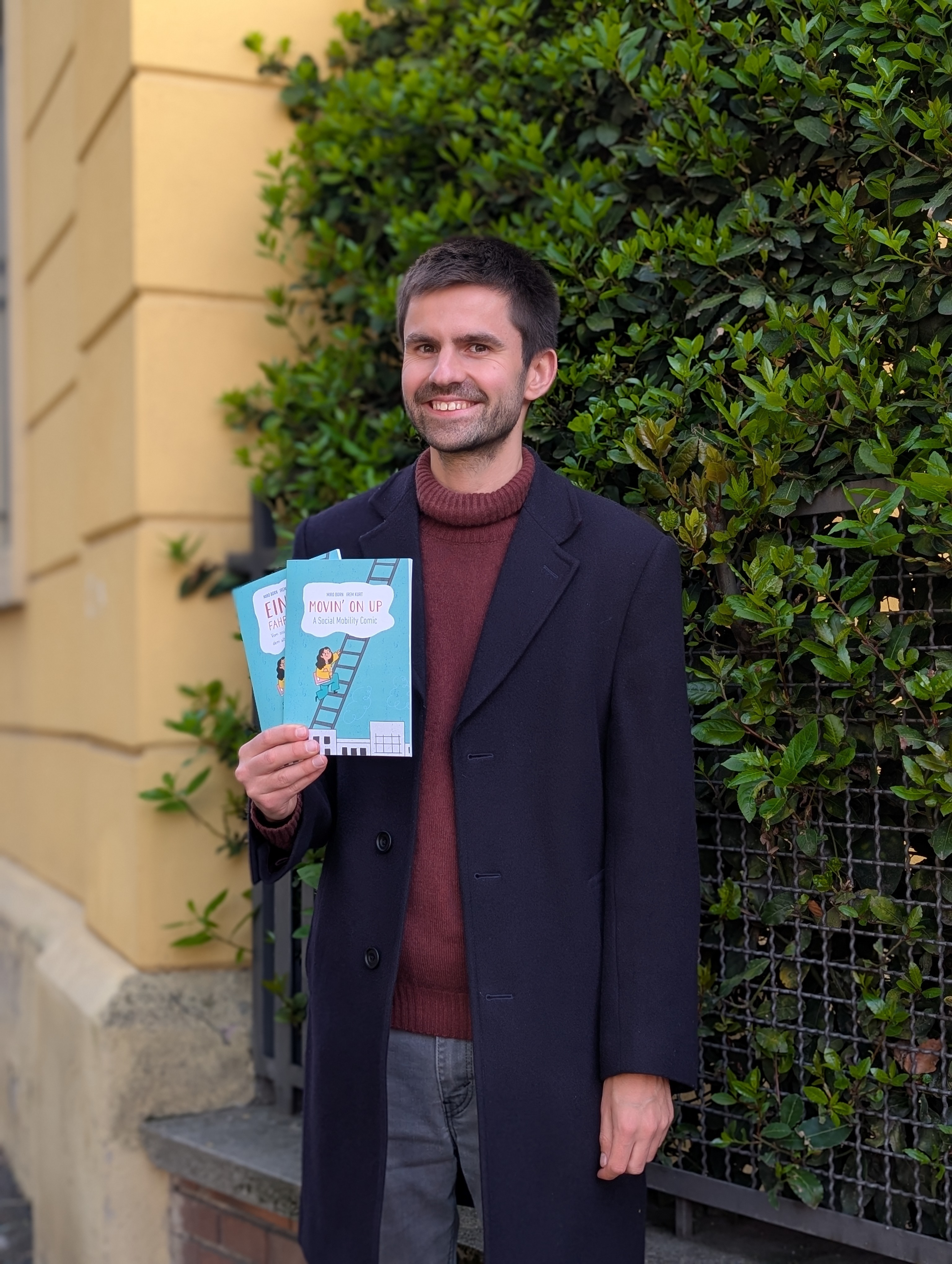 a man stands and smiles at the camera, holding a book