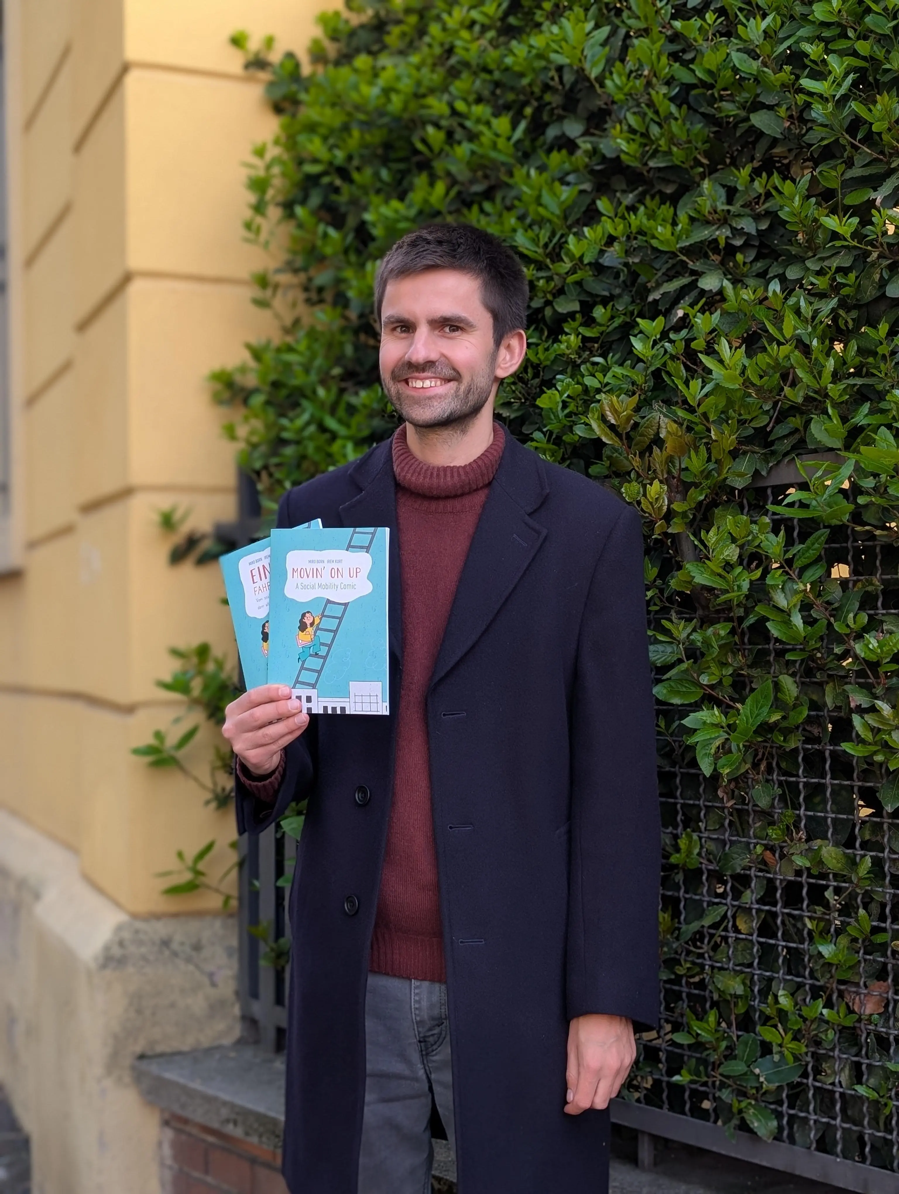 a man stands and smiles at the camera, holding a book