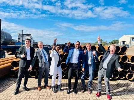 Six people in suits standing in front of copper coils in Mozambique. Deep blue sky.