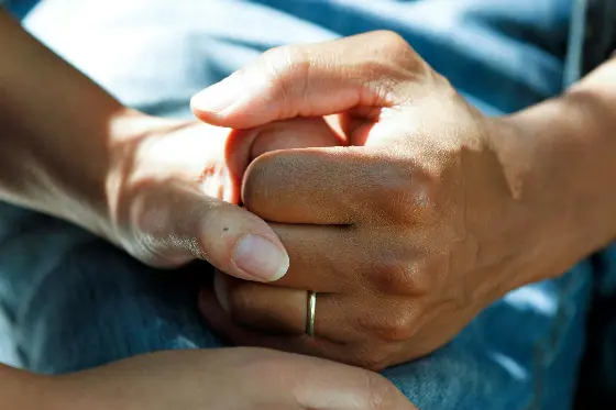 A man wearing a wedding ring holds a woman's hand.