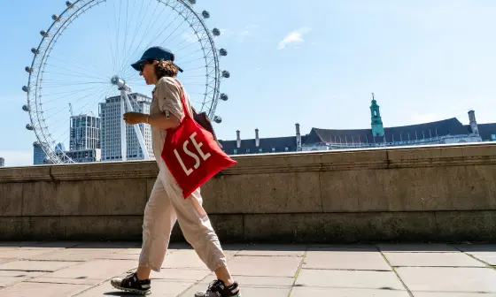 A person walking past the London Eye with a LSE tote bag