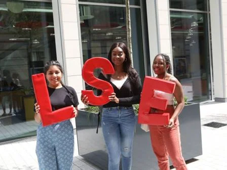Three students holding LSE logo