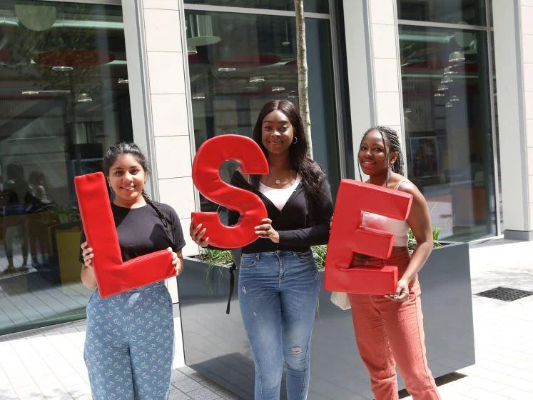 Three students holding LSE logo