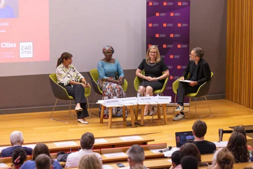 Four individual sit on chairs on stage during a panel discussion. Those people are; Anne Hidalgo, former Mayor of Paris; Yvonne Aki-Sawyerr, Mayor of Freetown; Kate Gallego, Mayor of Phoenix, and Professor Philipp Rode.