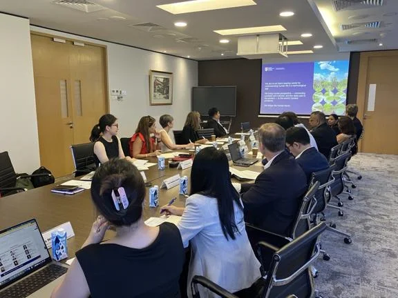 Individuals sitting at a long table in a meeting room watching a presentation.