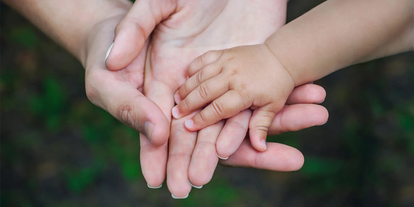 Baby's hand in the overlaid palms of two adults