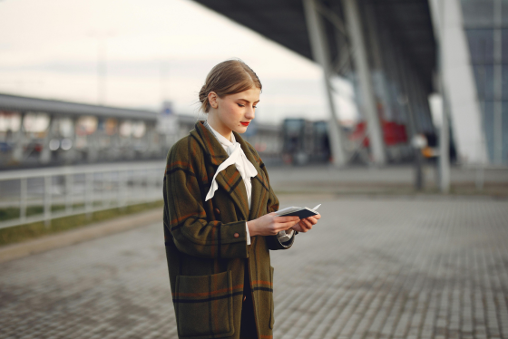Professional woman in plaid coat examining passport at airport terminal