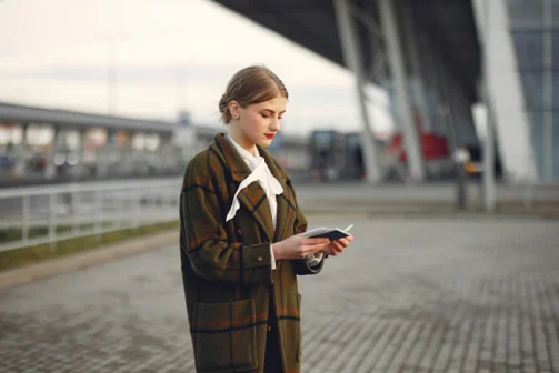 Professional woman in plaid coat examining passport at airport terminal