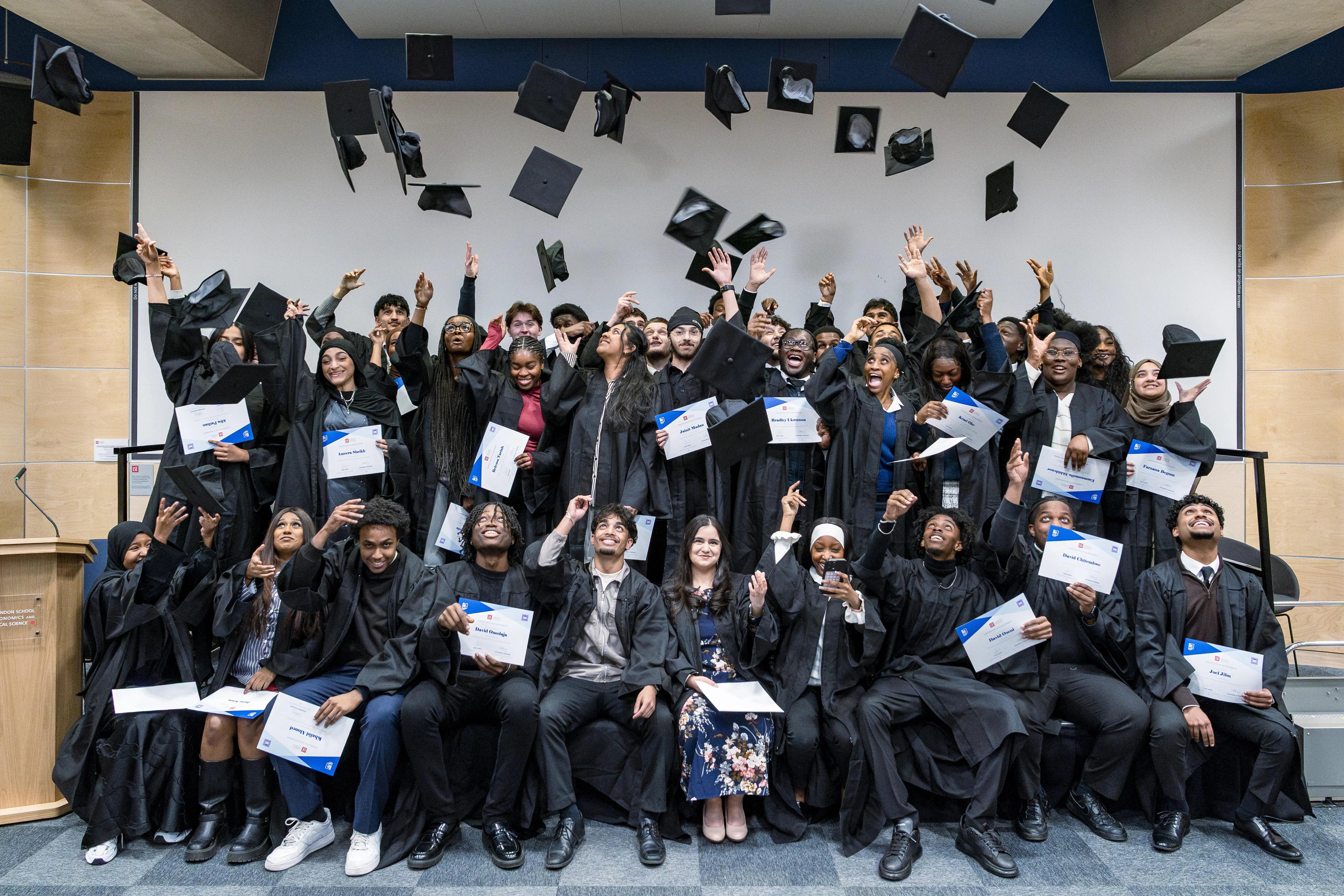 A group of pupils from the The Pathways to Banking and Finance cohort 2025 dressed in graduation gowns throwing their caps in the air.