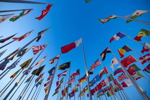 Multiple national flags from around the world against a bright blue sky